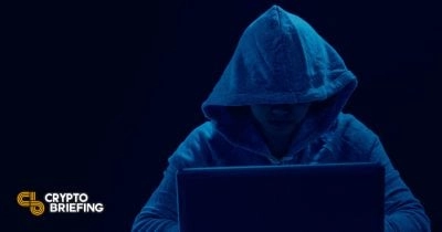 Hacker in a dark hoodie working on a laptop, suggesting potential cybercrime or security breach related to cryptocurrency.