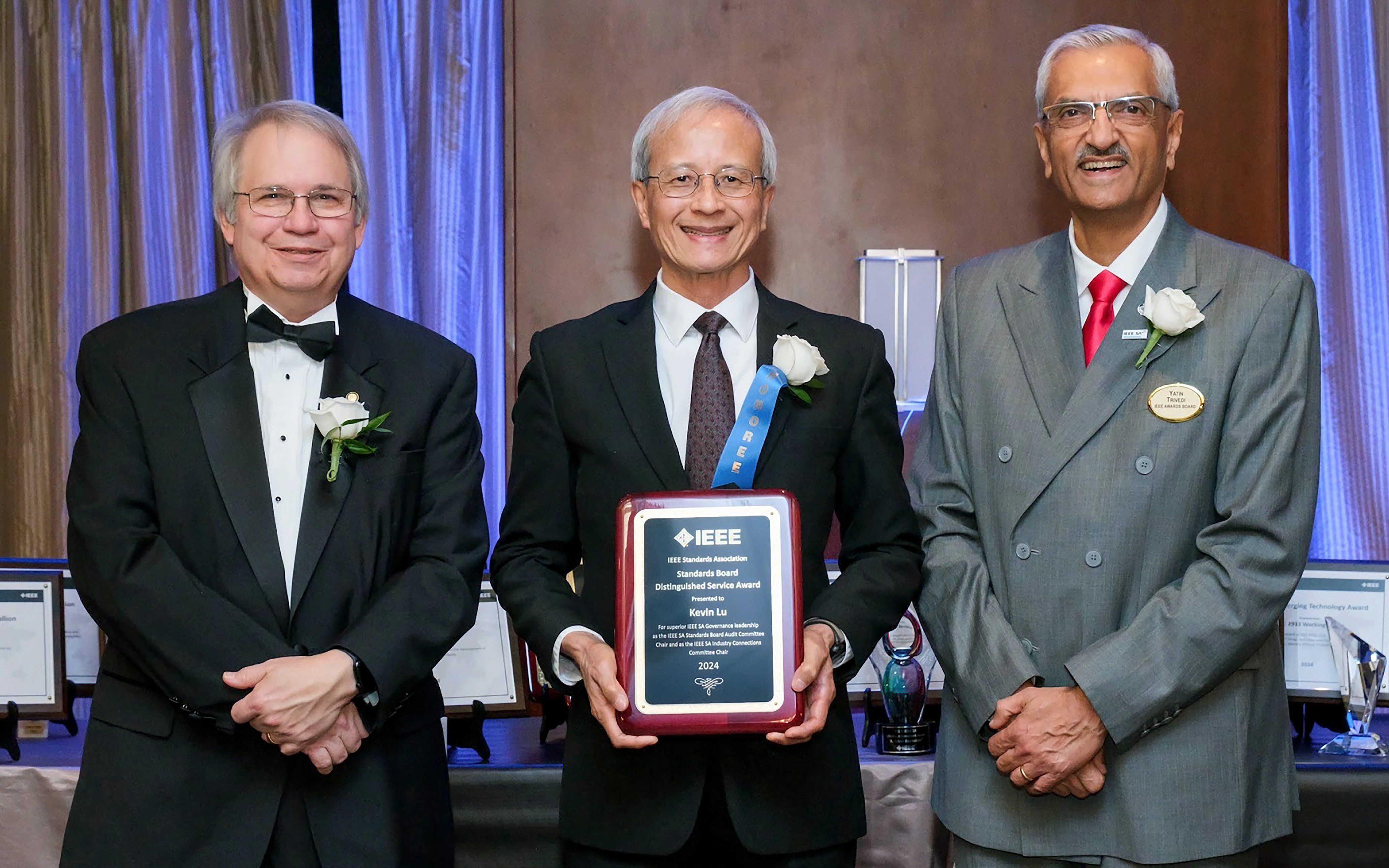 Kevin Lu holding an IEEE plaque for Distinguished Service. He is posing in a suit and tie between James E. Matthews and Yatin Trivedi.