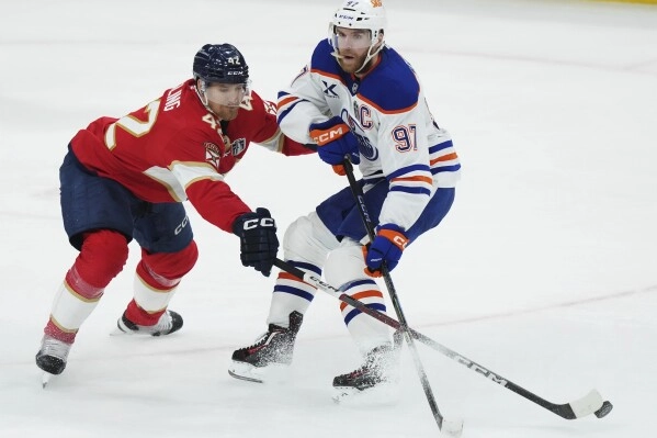 Florida Panthers' Gustav Forsling (42) pokes the puck away from Edmonton Oilers' Connor McDavid (97) during the second period in Game 3 of the NHL hockey Stanley Cup finals in Sunrise, Fla., Monday, June 9, 2025. (Nathan Denette/The Canadian Press via AP)