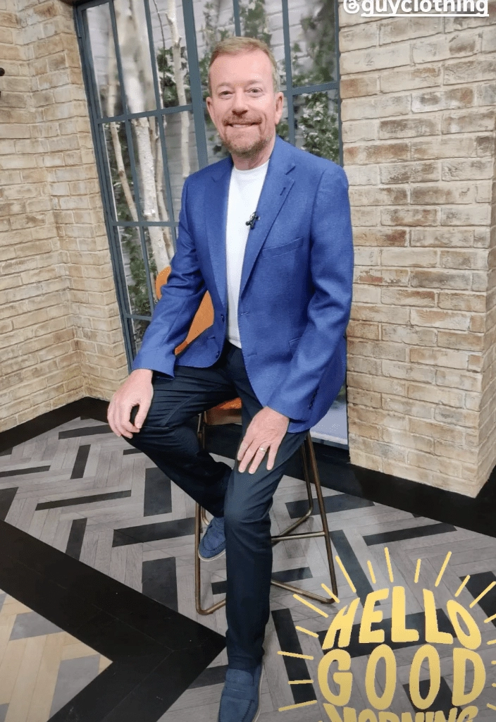 Man in blue blazer sitting on a stool.