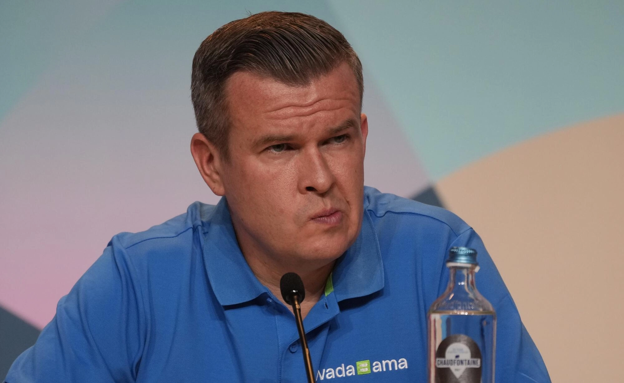 a man sits at a microphone with a furrowed brow and pursed lips