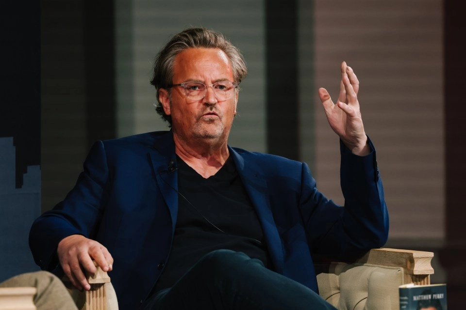 A man in a blue blazer gestures while seated.
