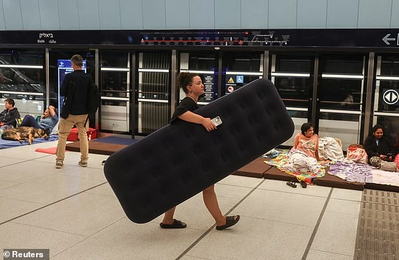 A woman walks with an inflatable mattress as people rest inside an underground train station used as a shelter amid rounds of missile attacks from Iran to Israel in recent days, in Ramat Gan, Israel June 17, 2025. REUTERS/Ronen Zvulun