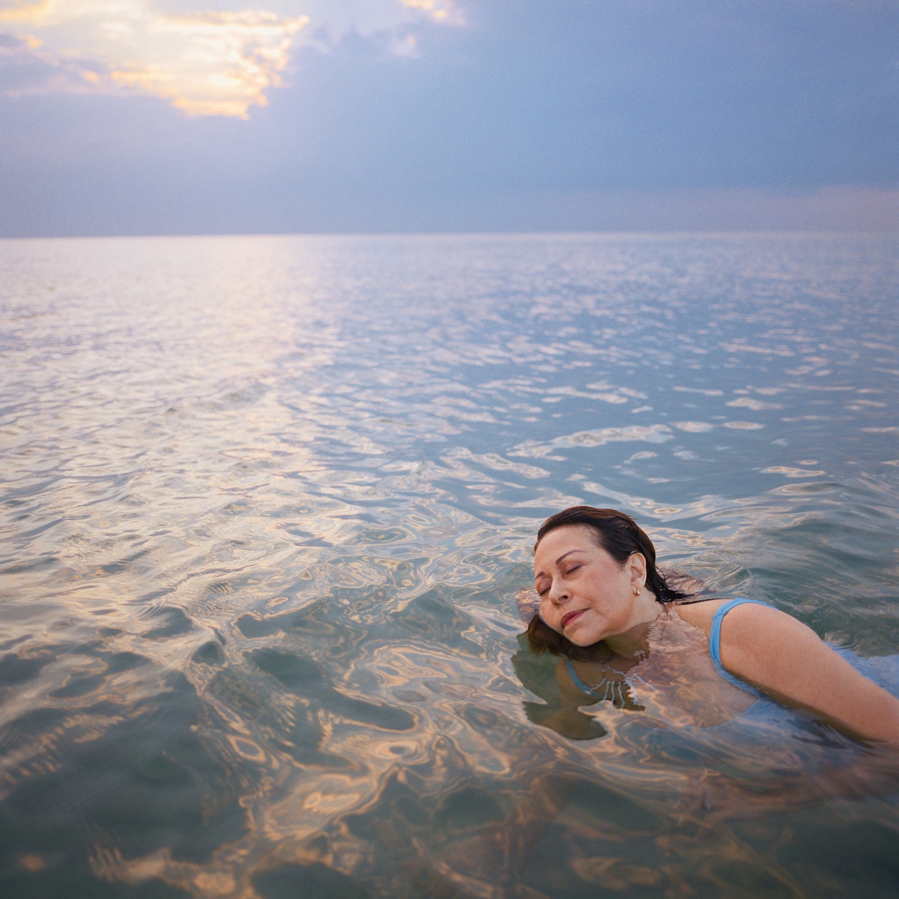 A woman closes her eyes and floats in the sea. The light is soft and the sky is a periwinkle color.