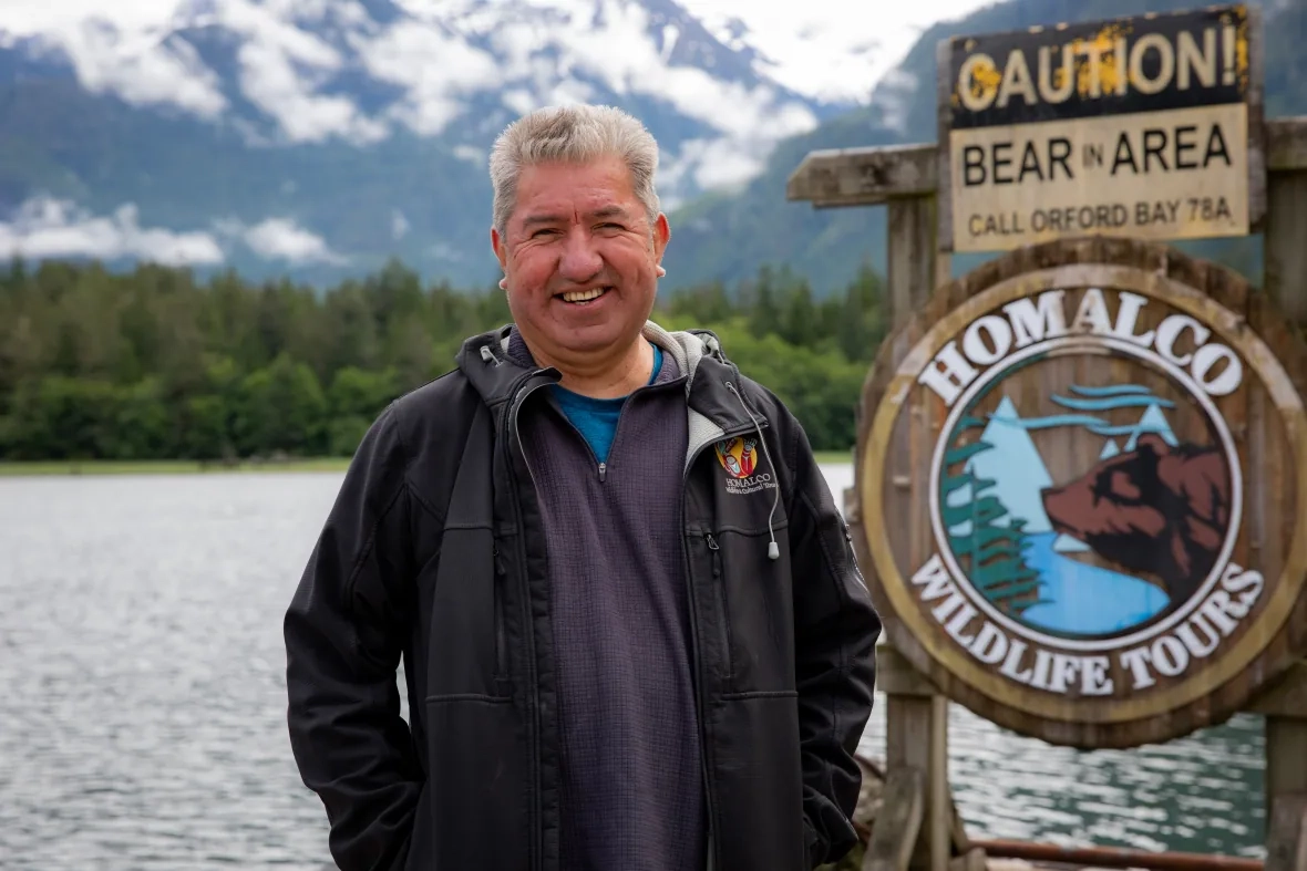 A smiling Indigenous man with white hair stands on a dock.