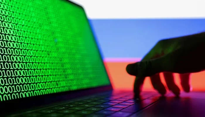 A hand is seen on a laptop with binary code displayed on the screen in front of Russian flag in this picture illustration taken August 19, 2022.  Reuters