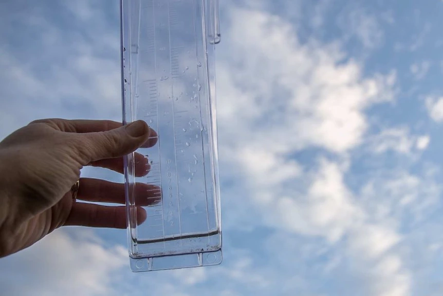 A hand holding a rain measurement gauge up to the sky.