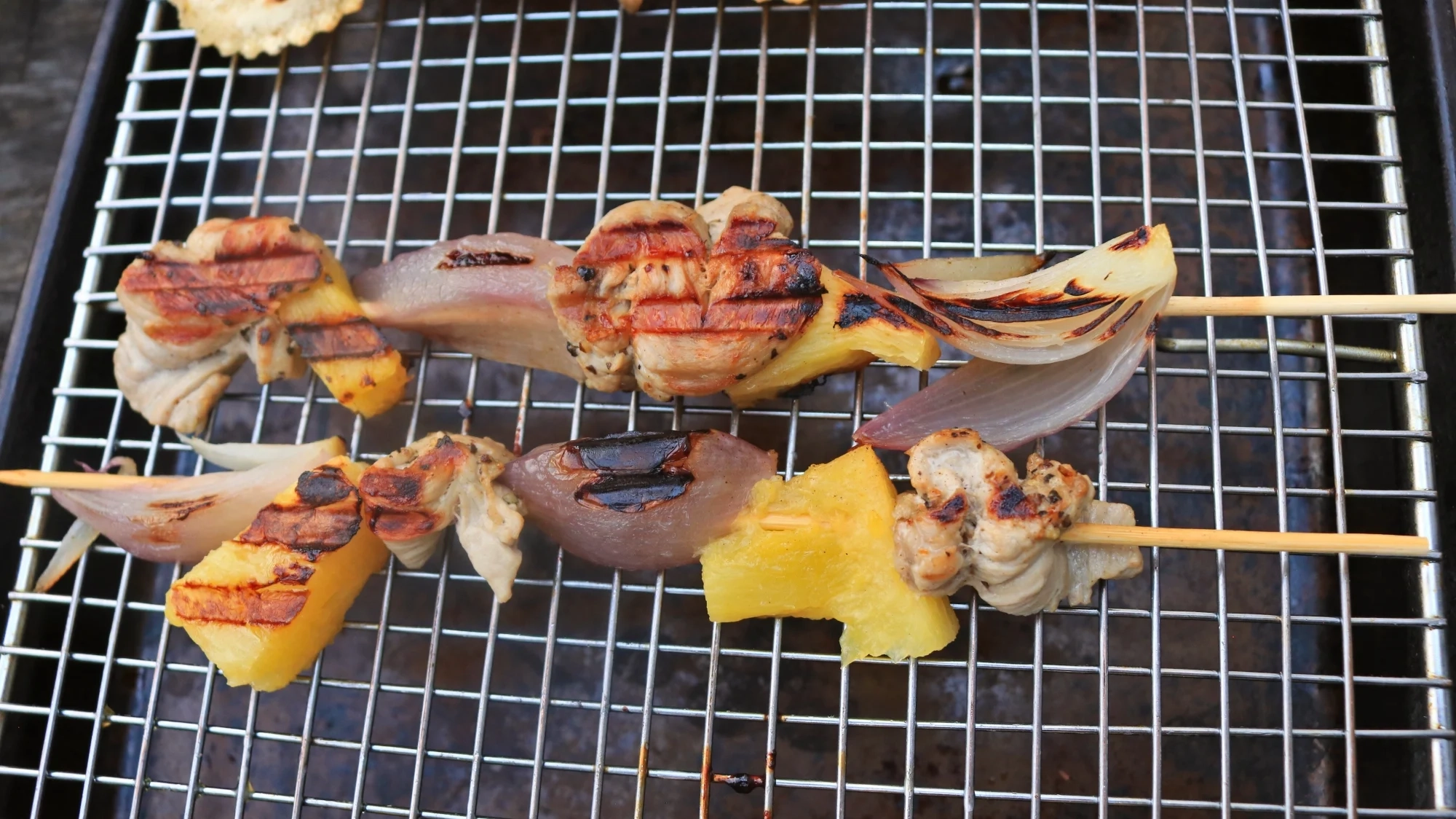Two skewers with pork, pineapple, and shallots.