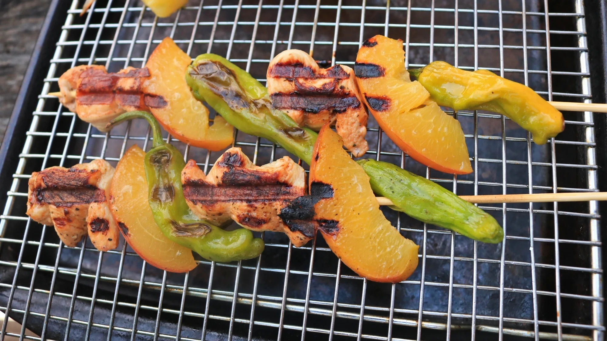 Two skewers with chicken, whole shishito peppers, and nectarine slices.