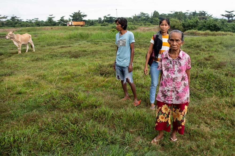 In this photo taken on May 24, 2025, Moharen Tambiling (L), his sister Alayma (C) and their mother stand on their coconut and rice farms next to stockpiled nickel ore at Maasin village in Brooke's Point, Palawan province. AFP pic