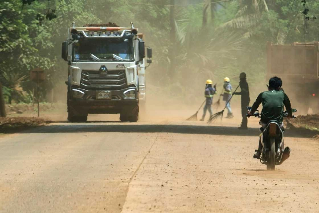 Workers armed with brooms, goggles, hats and scarves sweep an access road that carries 6,000 tonnes of ore destined for China each day