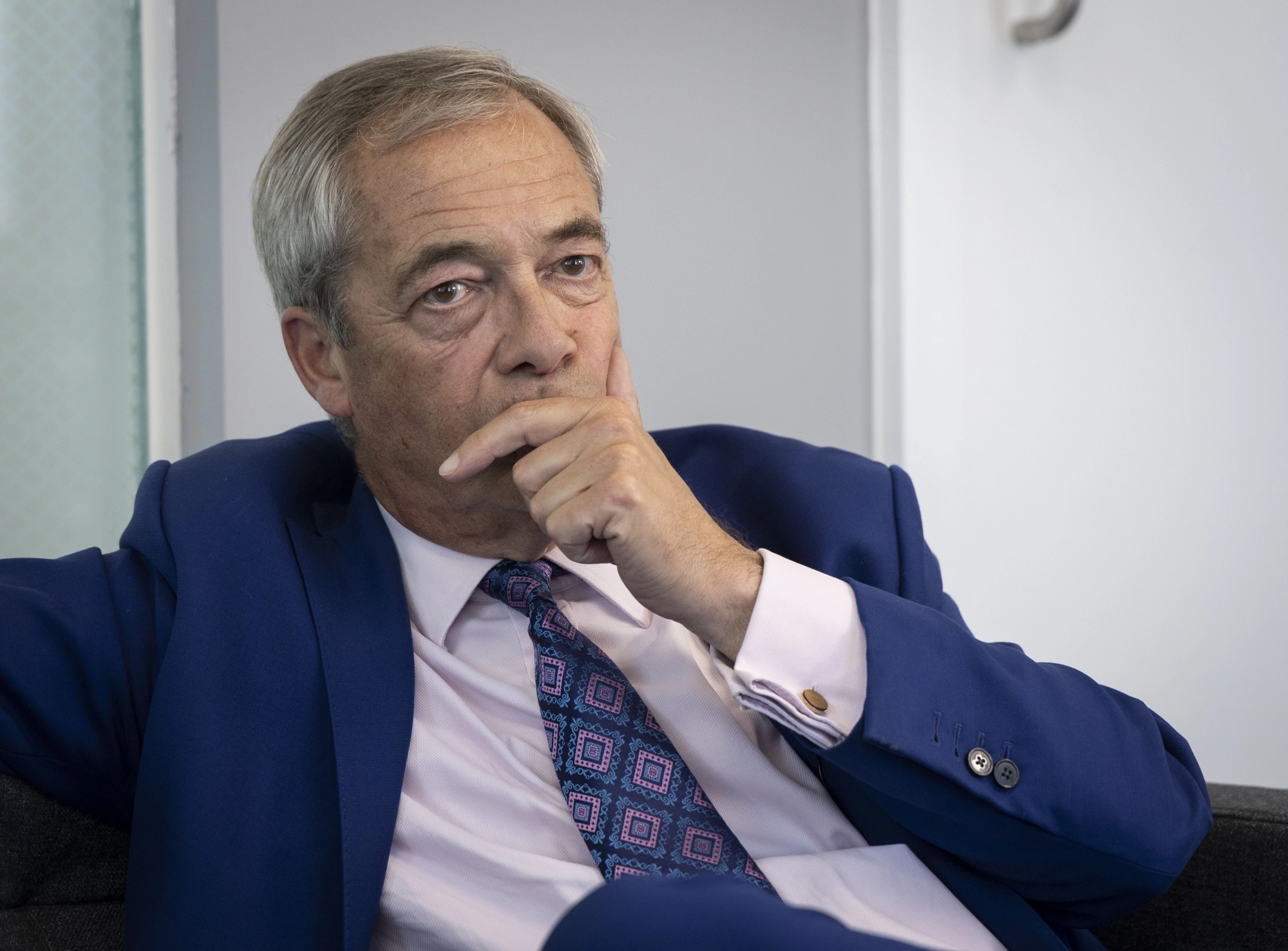 Nigel Farage in a blue suit, hand on chin.