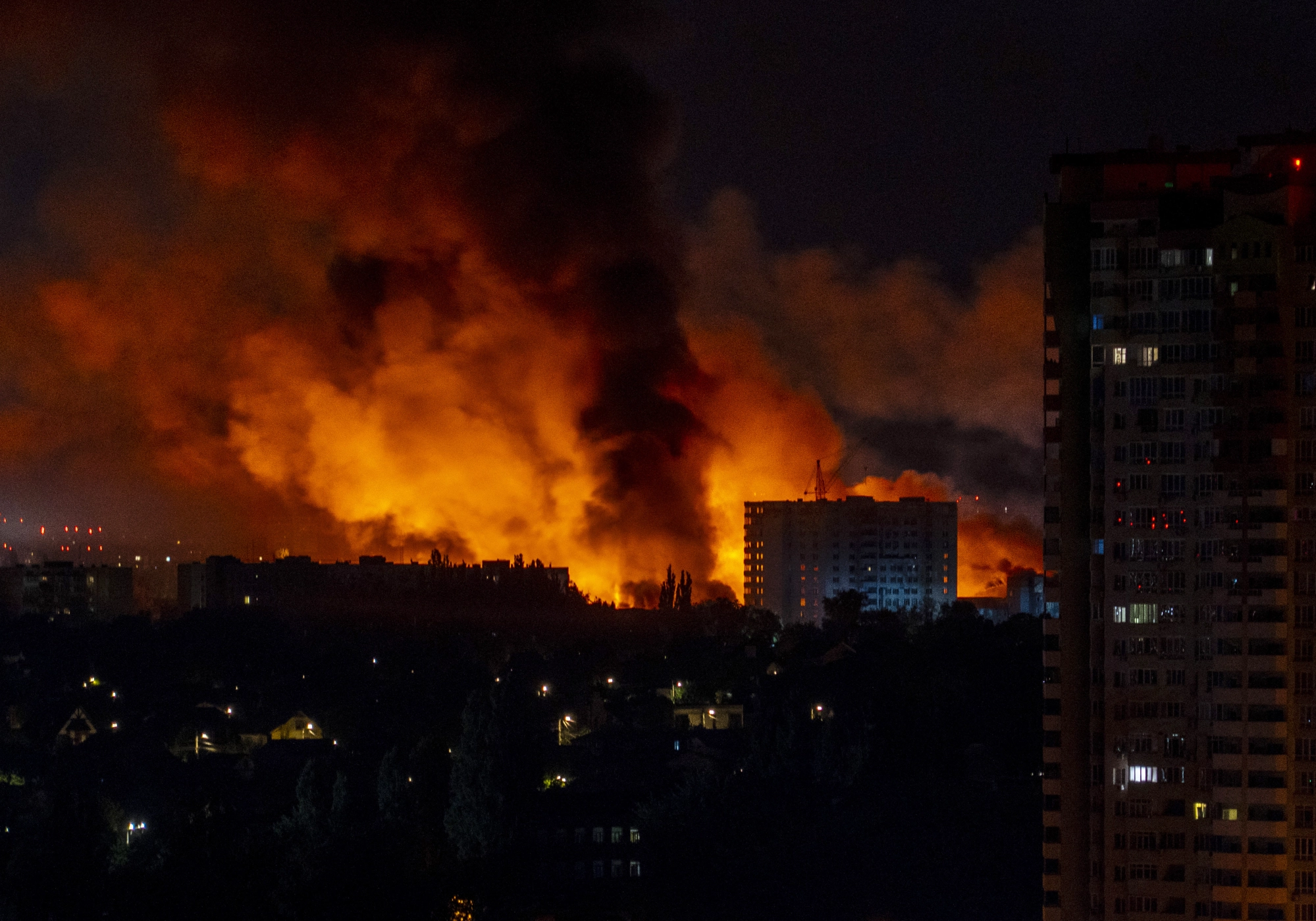 Nighttime photo of large fire engulfing buildings in a city.