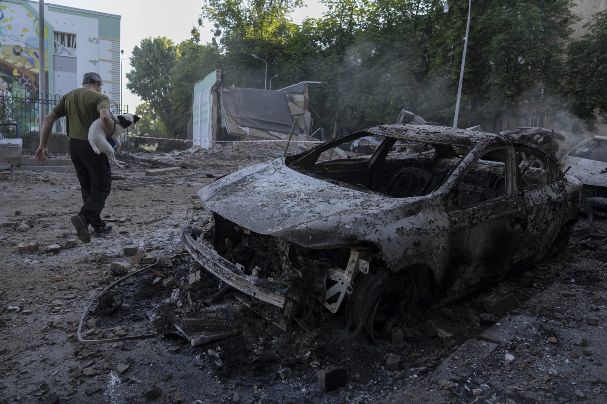 A man carries a dog past a burned-out car in war-torn Kyiv.