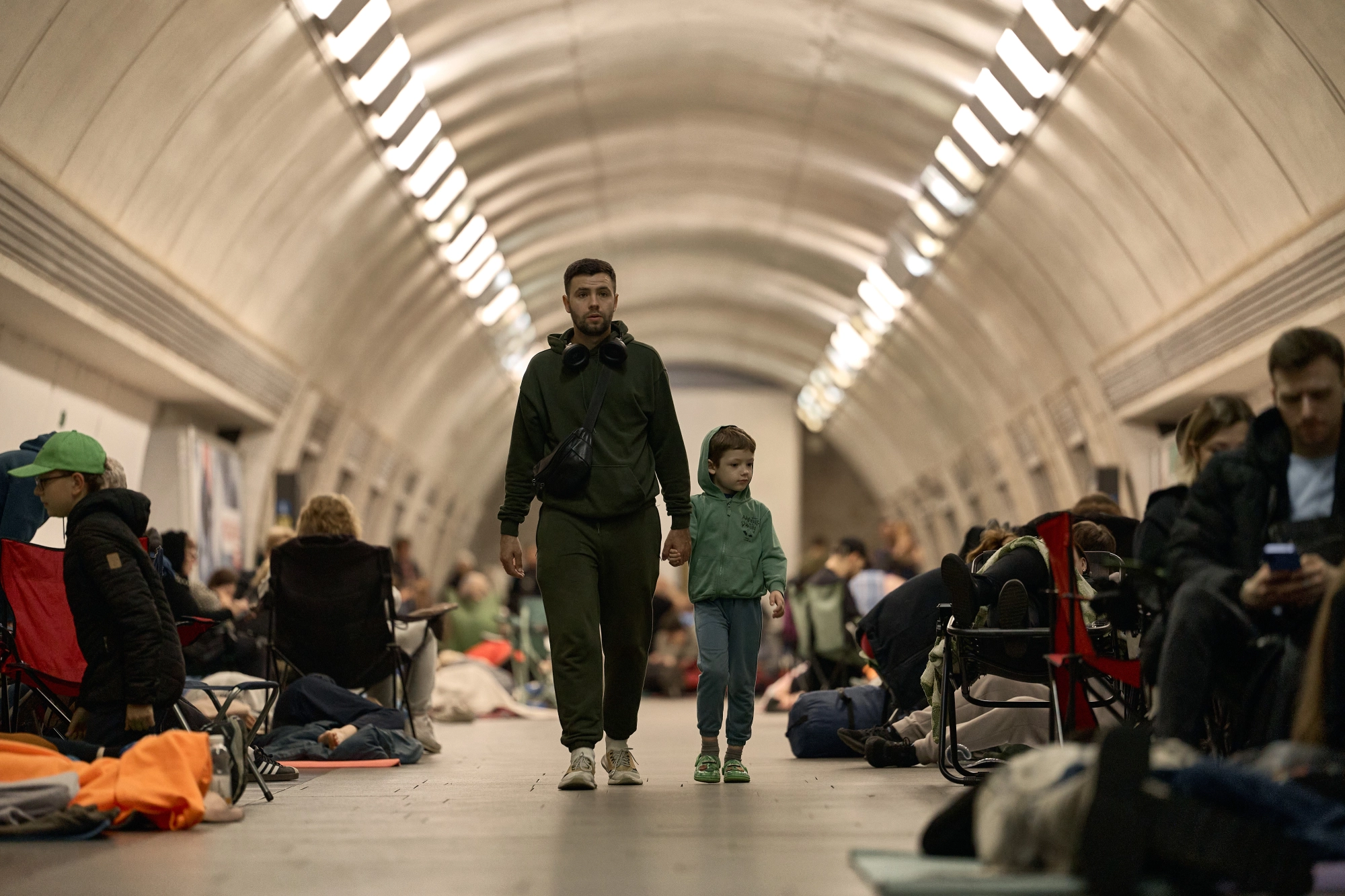 A man and child walk through a Kyiv metro station, where people are taking shelter.