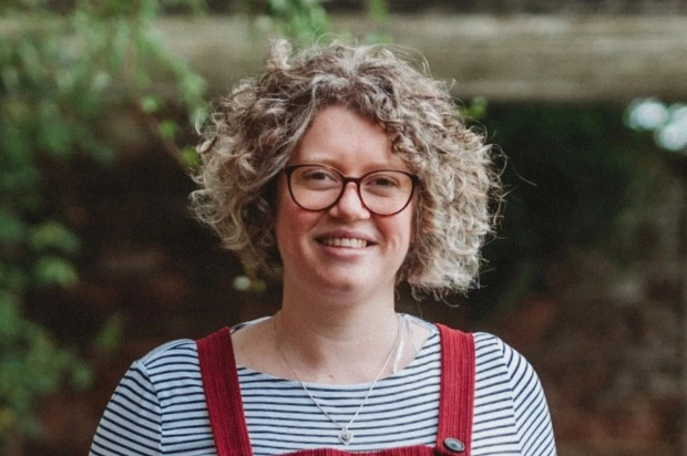 Woman in red overalls smiling under a pergola.