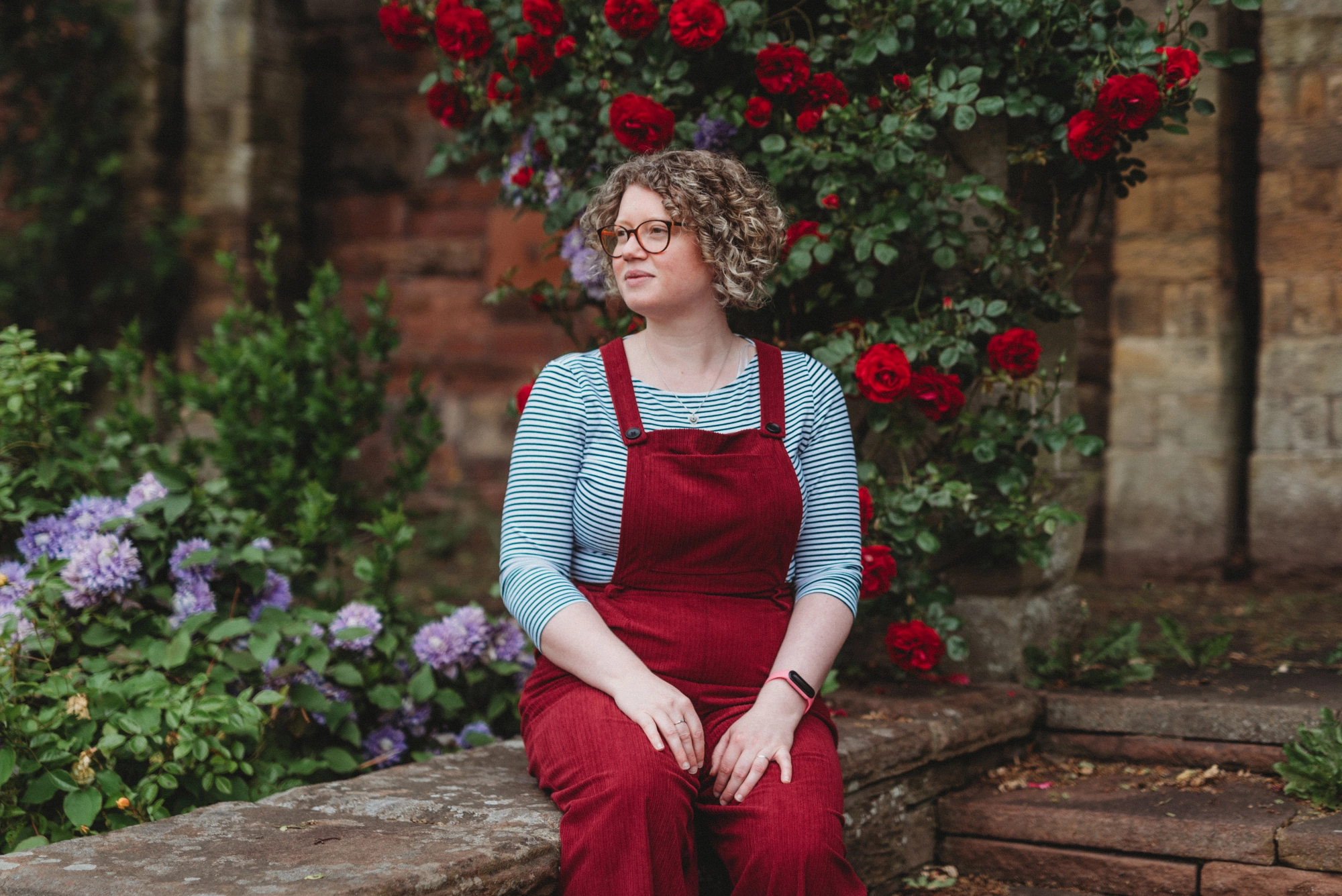 Woman in red overalls sits in a garden.