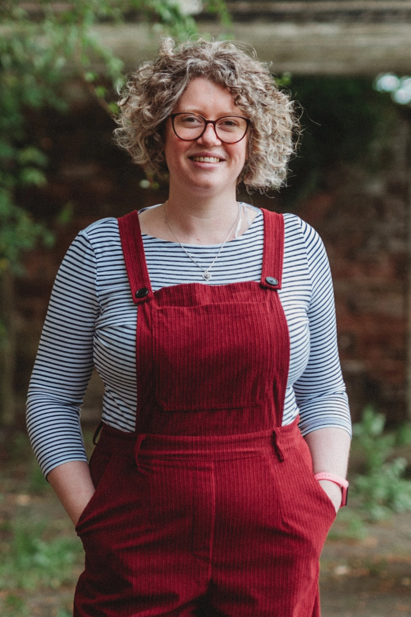 Woman in red overalls smiling under a pergola.