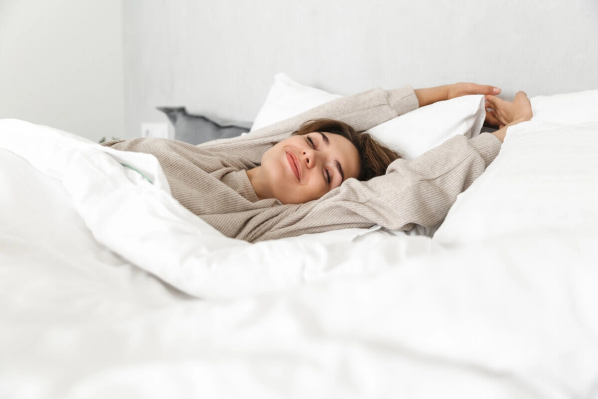 Happy woman waking up from sleep in her bed stretching