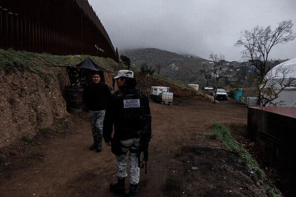 Members of the Mexican National Guard in March at their encampment next to the border. Cars are parked in the dirt, and fog hugs a nearby hillside.