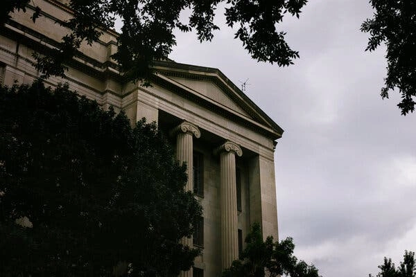 The outside of a classical looking building with columns on a cloudy day.