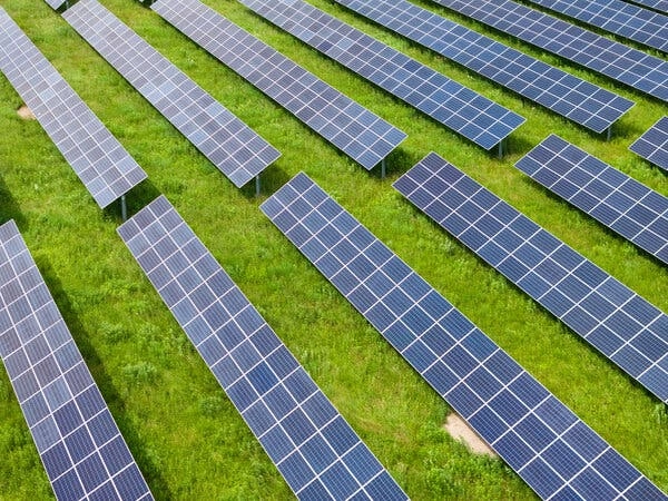 An array of solar panels lie on a green, grassy field.