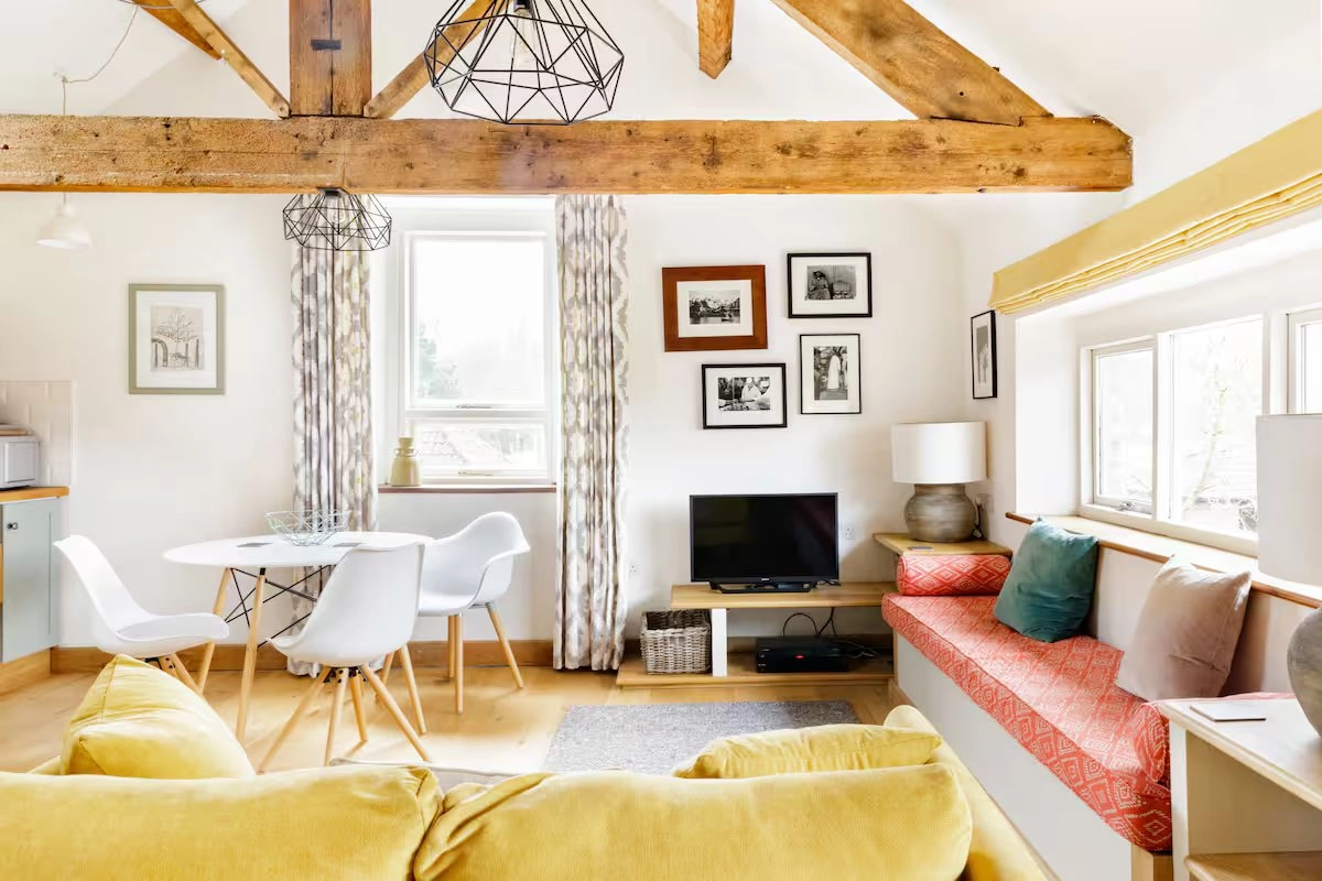 Converted granary living room with exposed beams, yellow sofa, and window seat.