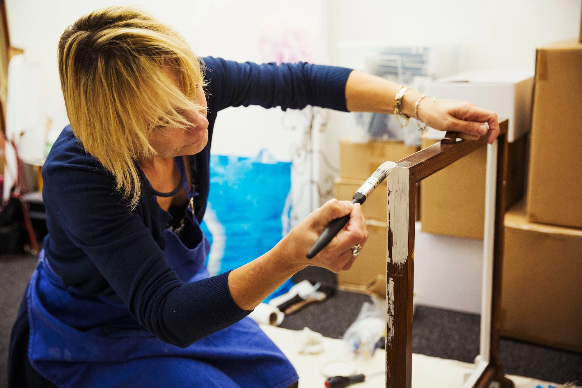 A woman working on a wooden frame with a paintbrush, upcycling wooden objects.