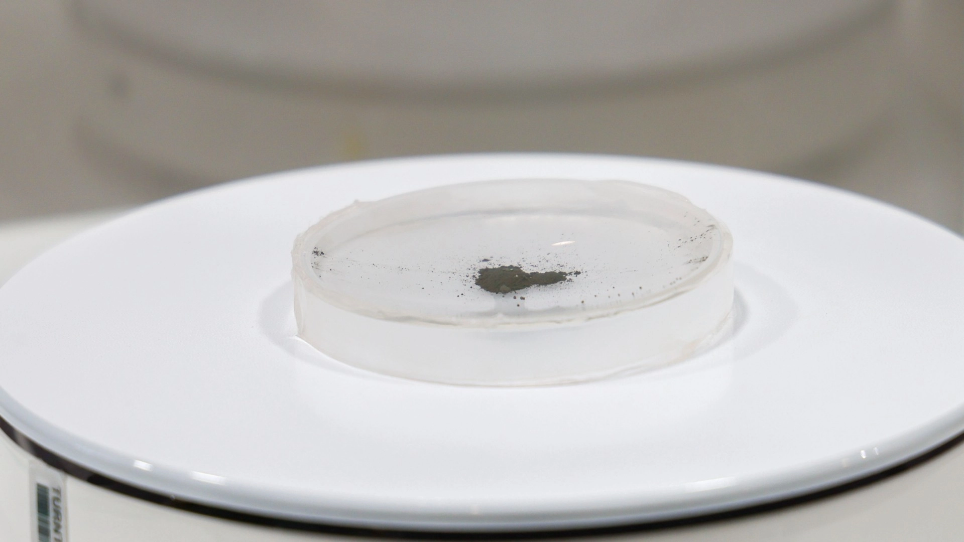 a small sample of grey soil in a glass dish on a white display stand