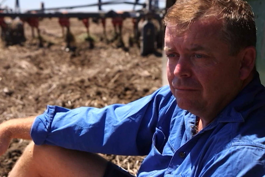 Farmer, Chris Lamey, leans against his harvester in a ploughed field