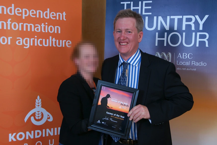 John Norman holds a framed certificate at the 2011 farmer of the year awards.