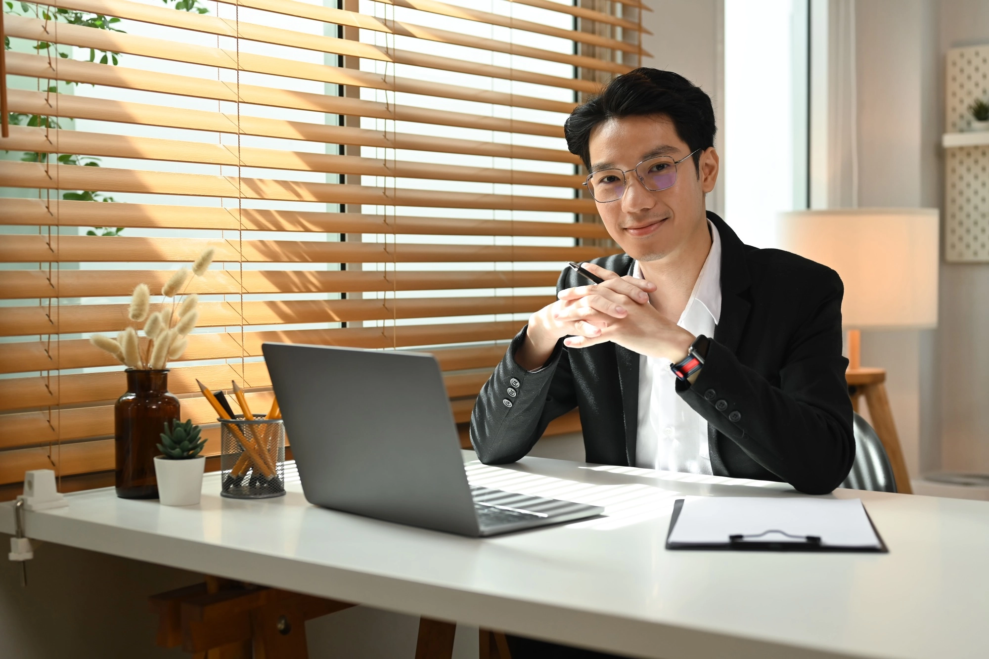 Smiling asian male entrepreneur sitting front of laptop computer at personal office.