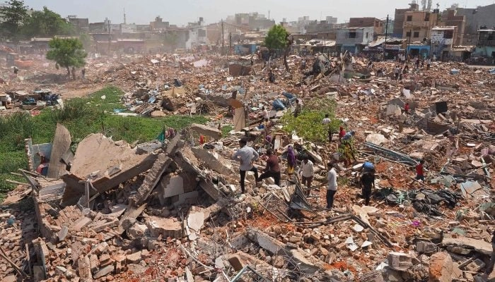 People stand amid the debris of a razed residential settlement who the authorities say belongs to illegal Bangladeshi nationals, near Chandola Lake in Ahmedabad on May 20, 2025.  AFP