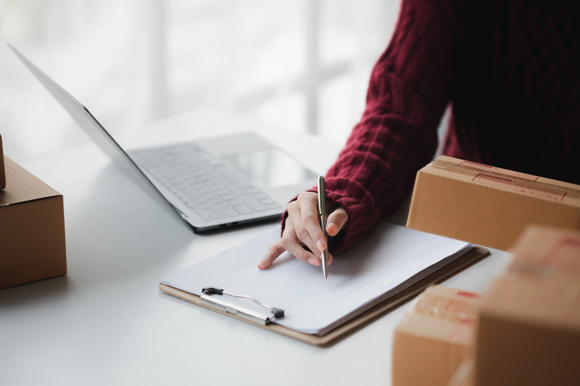 A person is writing down sales data in a notebook, selling products online.