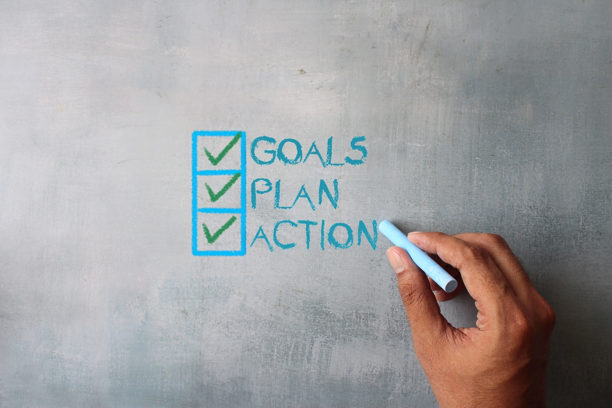 Top view image of hand writing word GOALS, PLAN and ACTION on chalkboard.