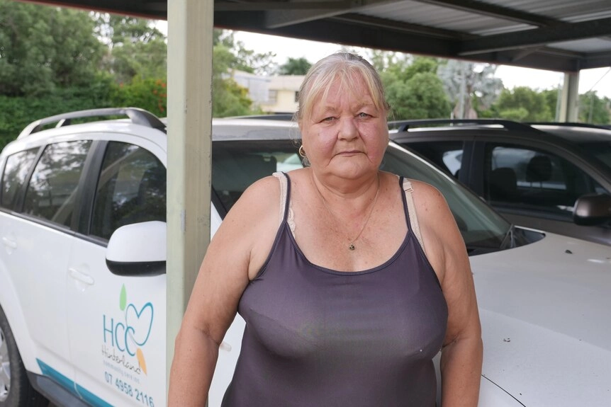 Serious woman with blond hair, looking into the camera with a white car in the backgrouund.
