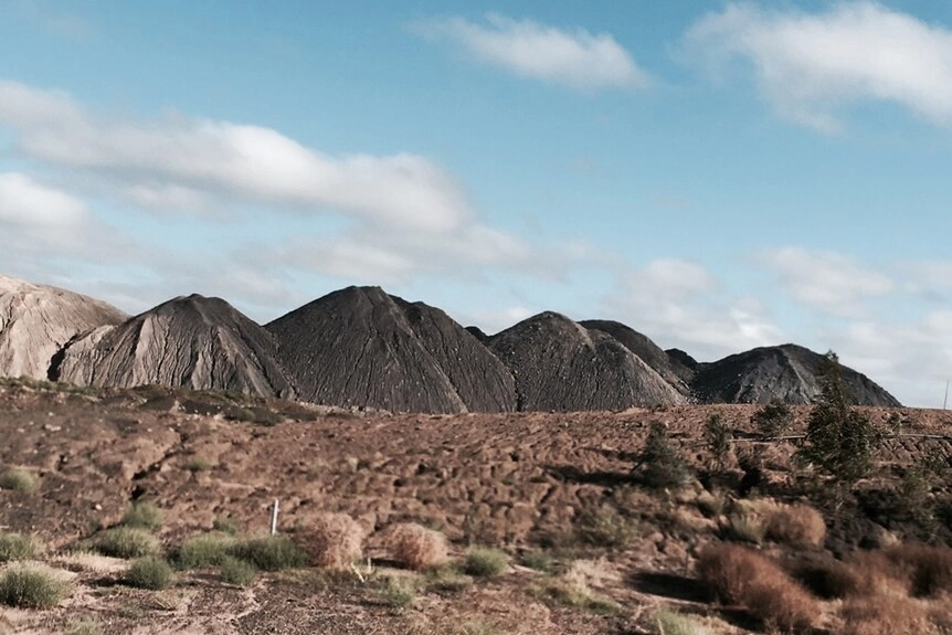Discarded piles of waste coal rise up from the flat, barren landscape outside a Central Queensland mining town.