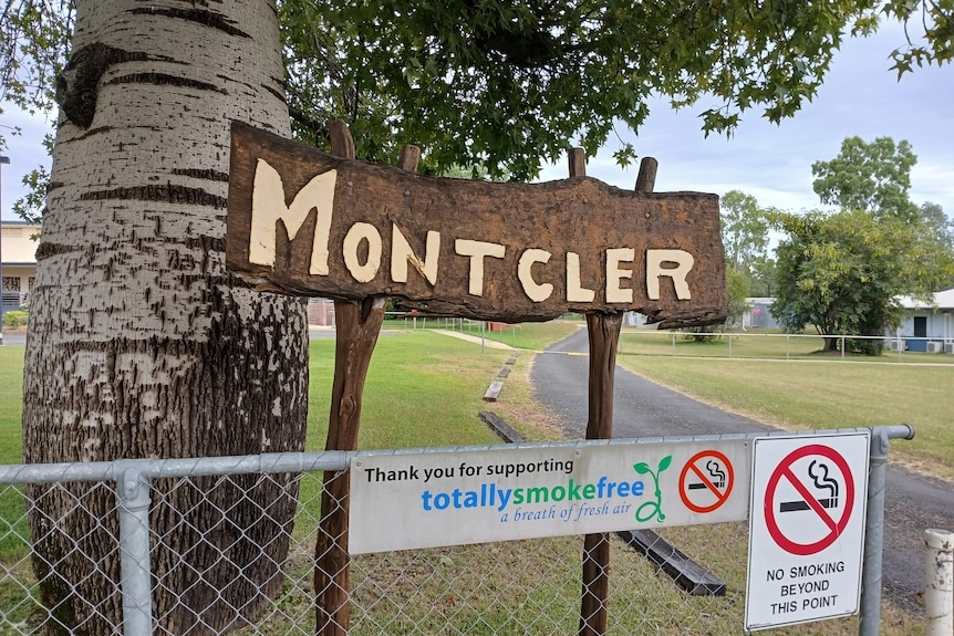 A wooden sign reading 'mont-cler', with a bulging tree behind it, a road in the background.