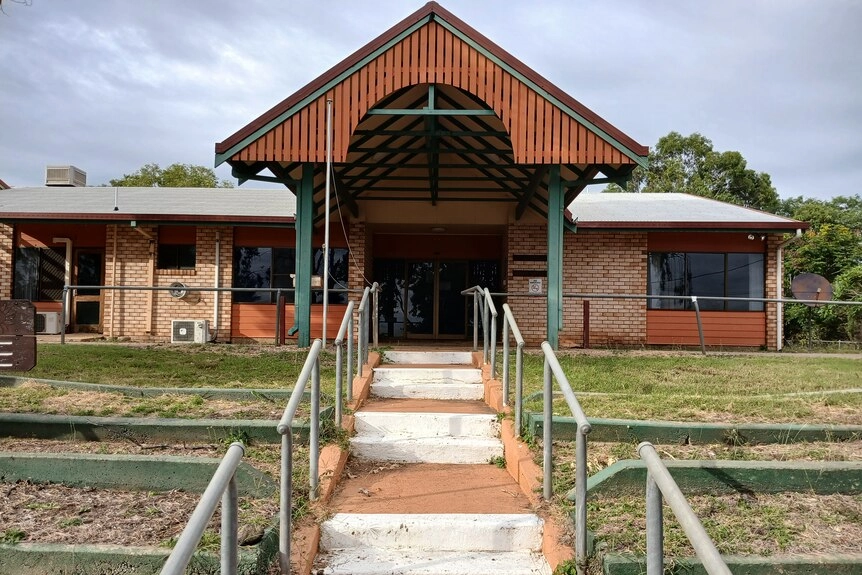Steps up to the a brick building with a large wooden entrance, metal railings framing the foreground.