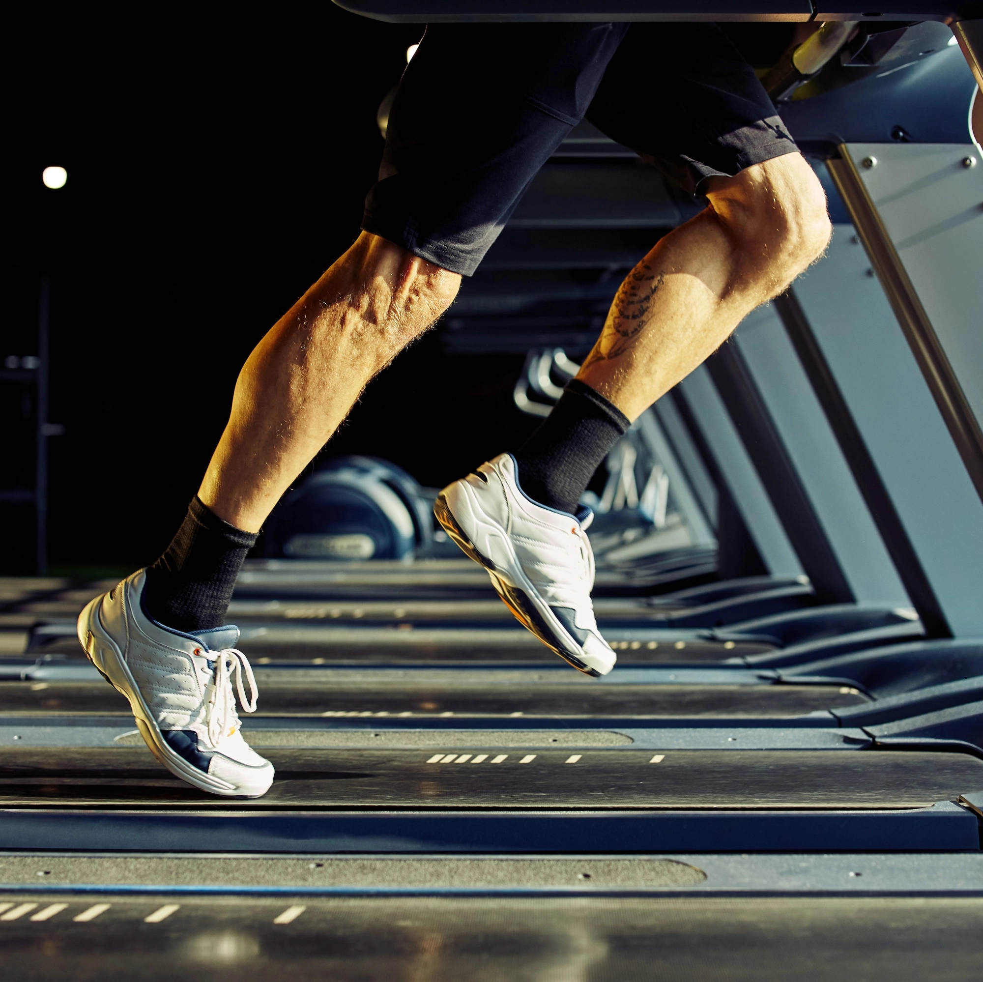 cropped shot of athletic man in sportswear running on a treadmill in a gym, focus on legs. sport and active lifestyle, training, cardio workout