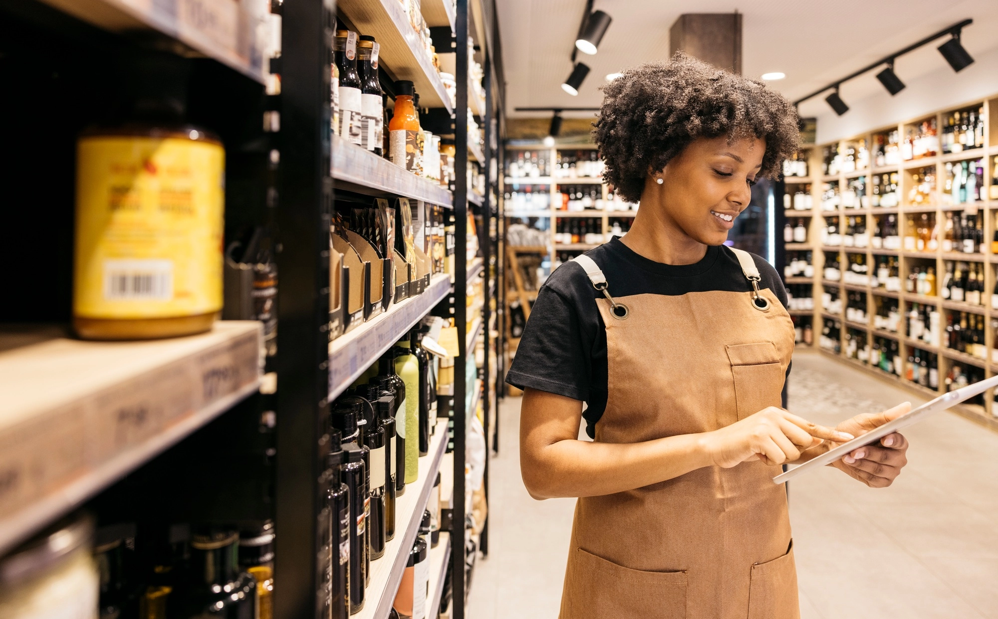 Supermarket employee managing inventory with digital tablet in wine and gourmet section