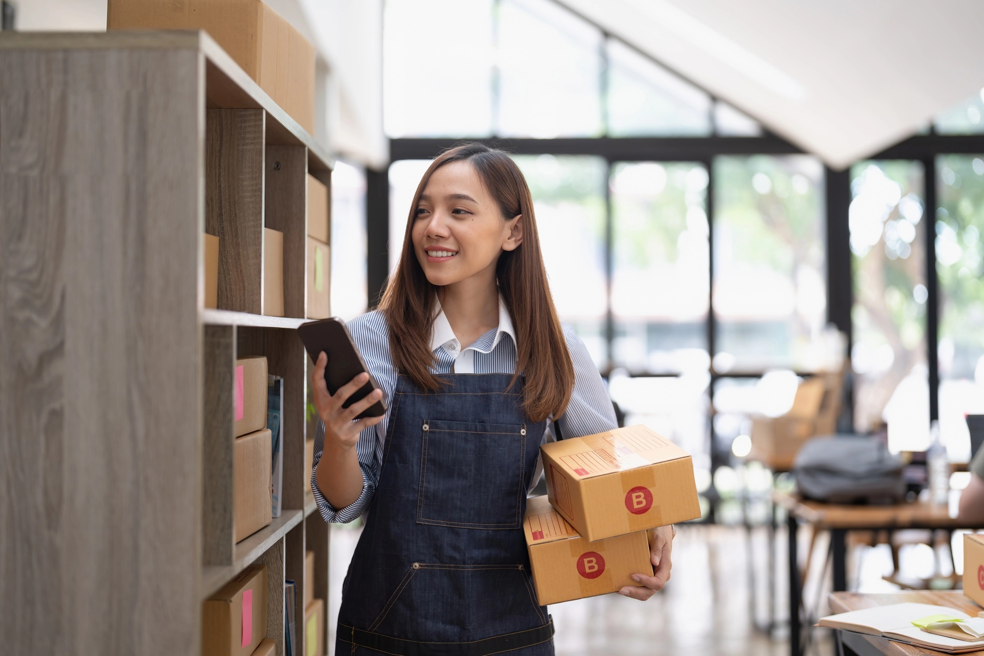 Attractive asian woman hold package box, using mobile phone checking stock order, startup SME