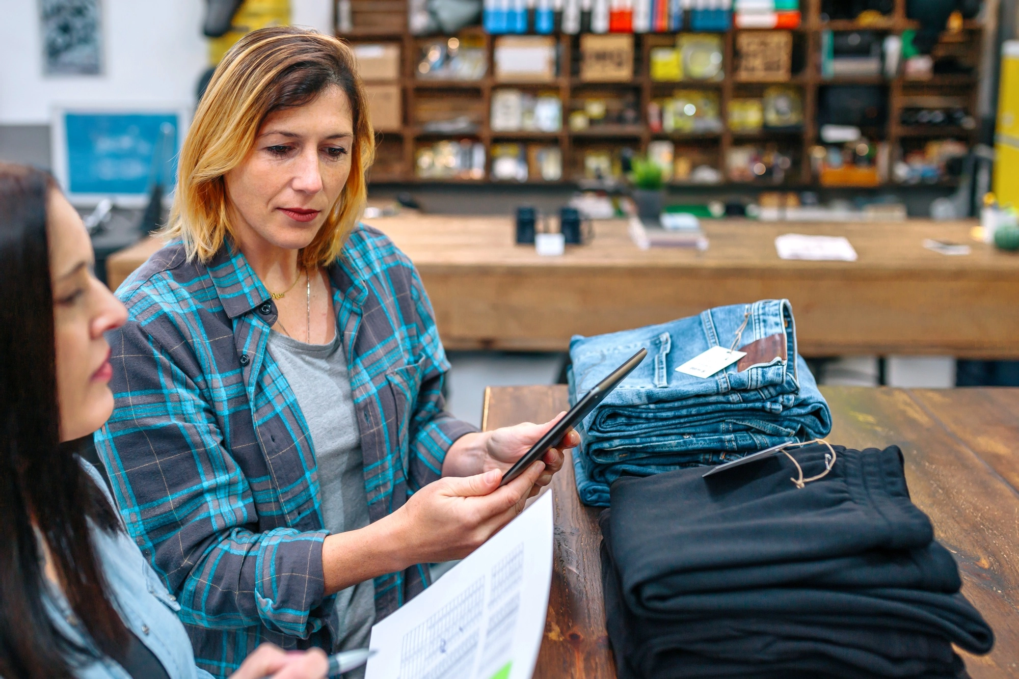 Portrait of blonde young woman holding digital tablet while checking clothes stock on local store