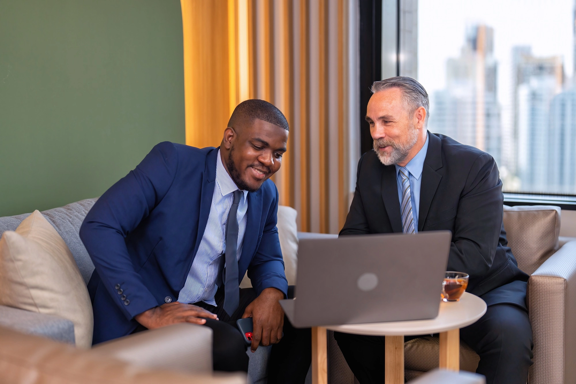 Two businessmen sitting on sofa working discuss on financial forecast together on laptop information