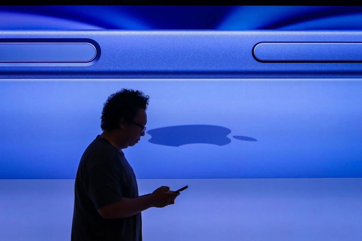 Person looking at phone in front of a blue Apple display.