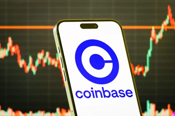 CHONGQING, CHINA - JULY 29: In this photo illustration, a smartphone displays the logo of Coinbase Global Inc. (NASDAQ: COIN), a leading cryptocurrency exchange and blockchain technology company, in front of a screen showing the company's latest stock market chart on July 29, 2025 in Chongqing, China. (Photo illustration by Cheng Xin/Getty Images)