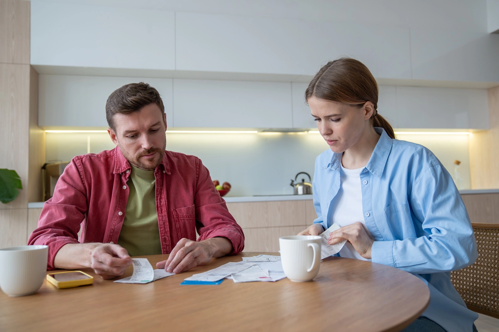 Thoughtful couple planning family budget, analysing, counting expenses on smartphone calculator