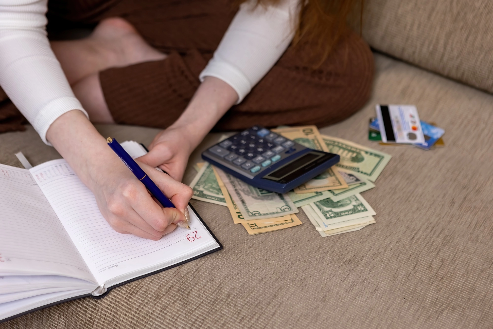 The girl is sitting on the couch and counting the budget. A woman plans expenses and records them in