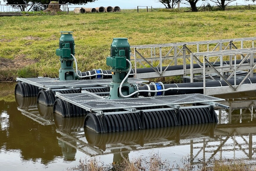 Two electric pumps float on a pontoon in the brown water of a farm dam.