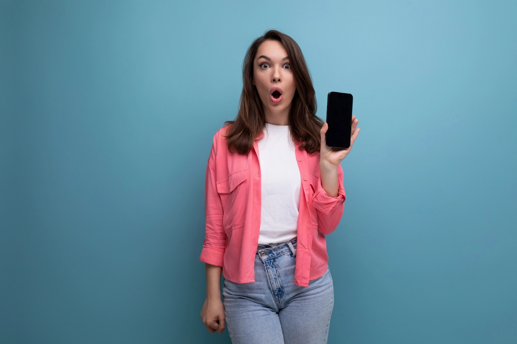 e-commerce business. brunette young woman in pink shirt and jeans holding smartphone with mockup on